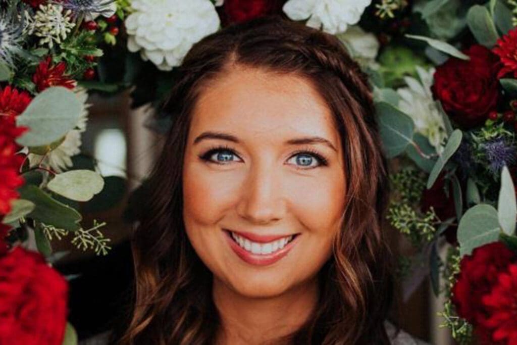 A woman with blue eyes and brown hair smiling, framed by colorful flowers.