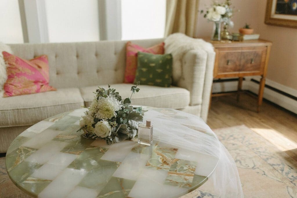A cozy living room with a floral arrangement on a round marble coffee table, flanked by a beige sofa and a chair.