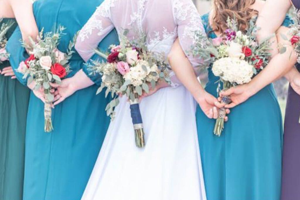 Four women in formal dresses hold colorful bouquets, with a focus on their clasped hands and the flowers.