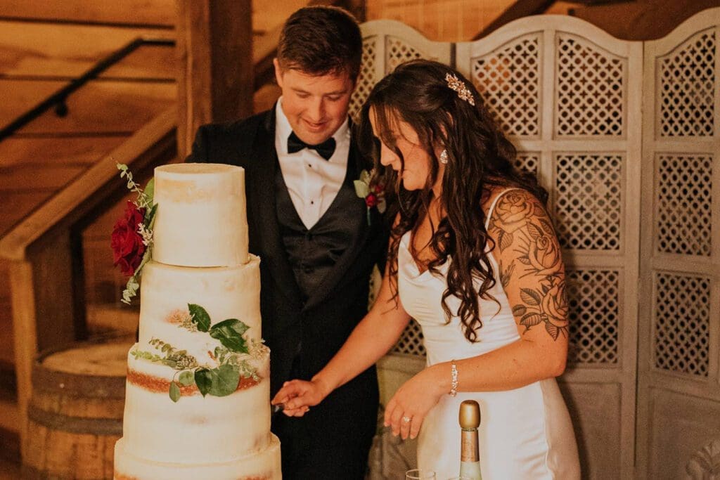 A bride and groom cut a multi-tiered wedding cake together in a warmly lit room.