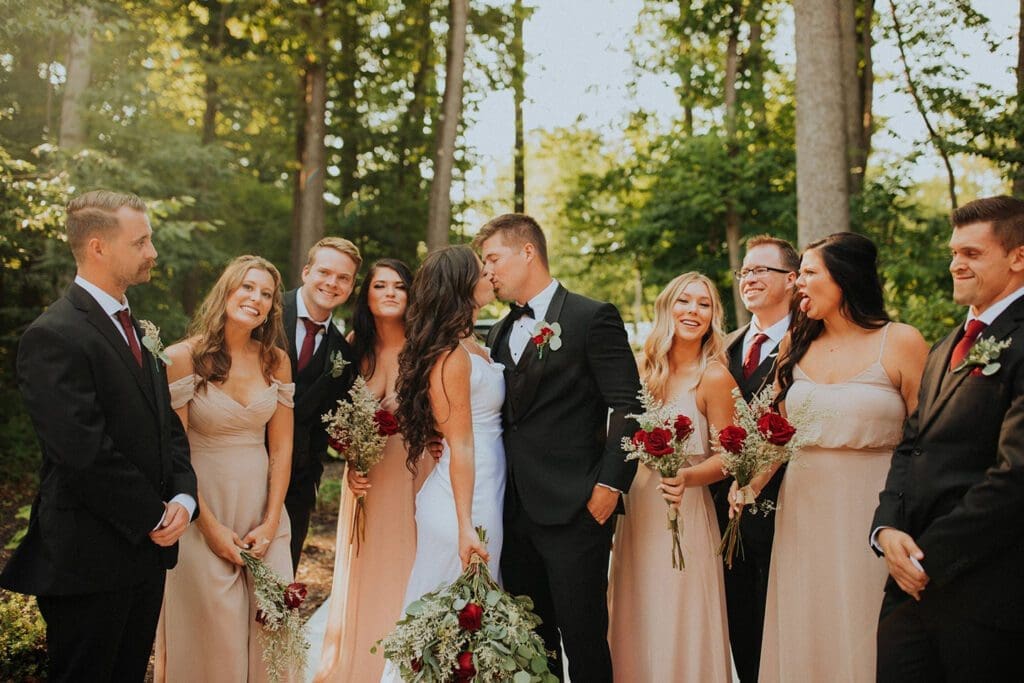 A wedding party with the bride and groom in the center, surrounded by bridesmaids and groomsmen in a forest setting.
