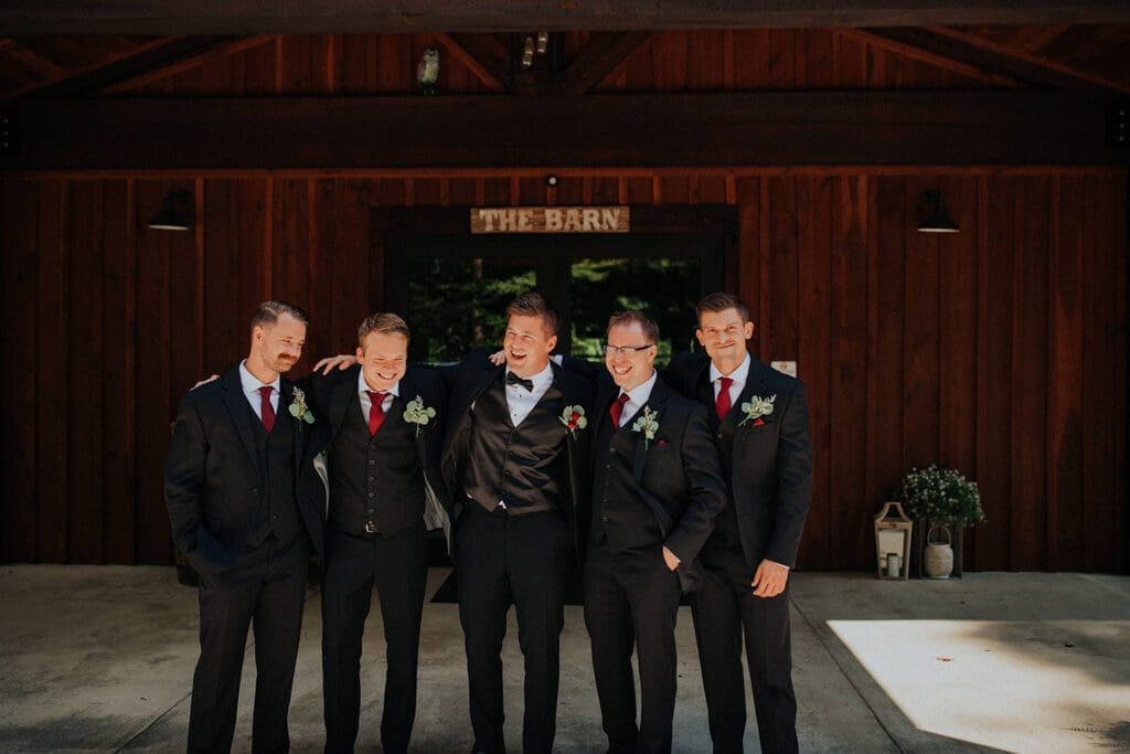Five men in suits laughing together in front of a barn labeled "the barn.