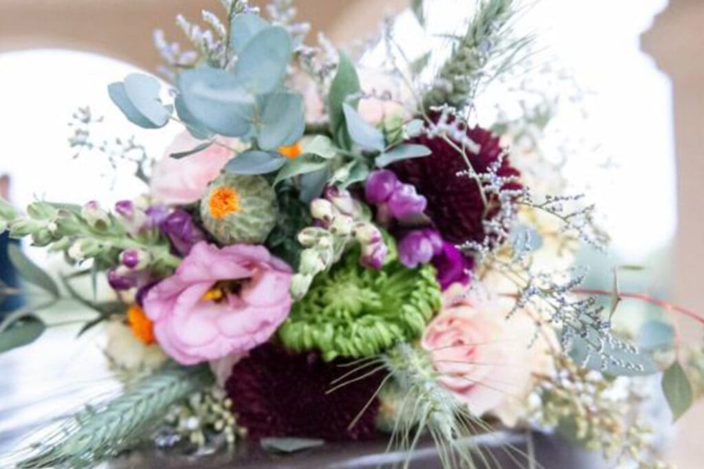 Close-up of a vibrant floral bouquet featuring an assortment of flowers including pink roses and dark red blossoms, surrounded by greenery.