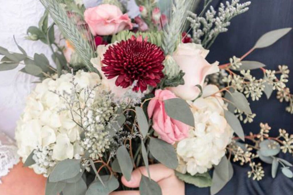 Close-up of a bridal bouquet featuring a variety of flowers including pink roses and a large burgundy bloom, held against a blue fabric background.