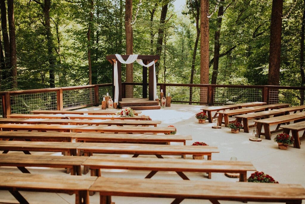 Outdoor wedding venue in a forest with wooden benches, a decorated altar, and floral arrangements.