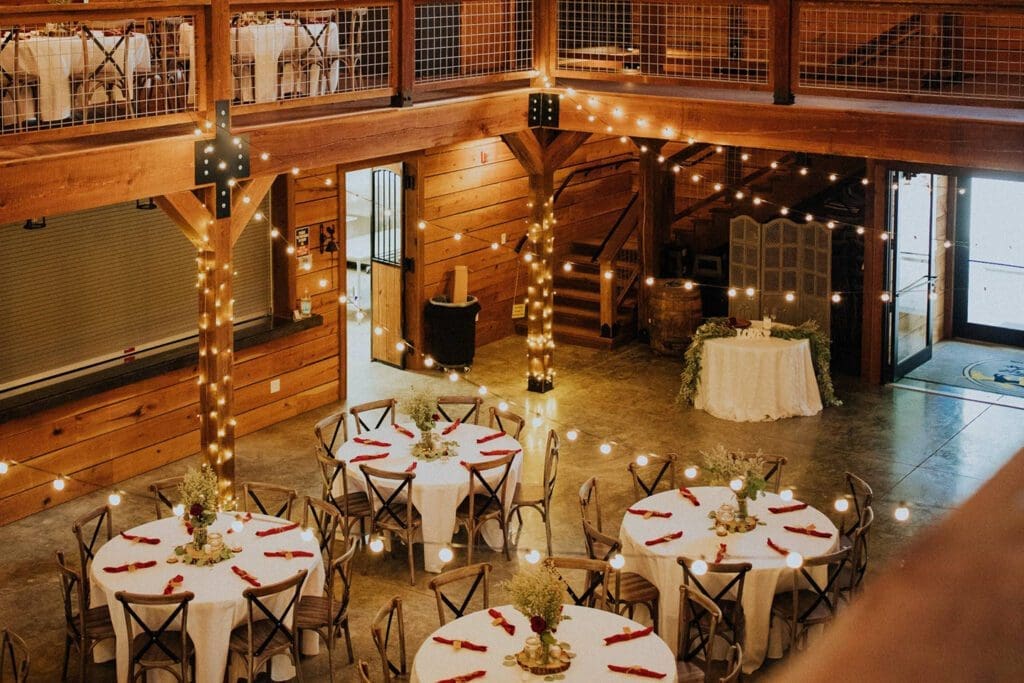 Elegant barn wedding venue decorated with string lights, wooden accents, and set tables ready for guests.